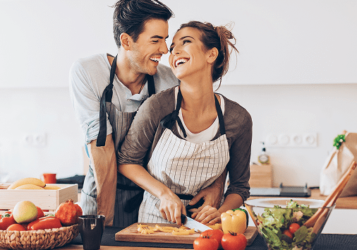 Smiling couple cooking together wearing aprons